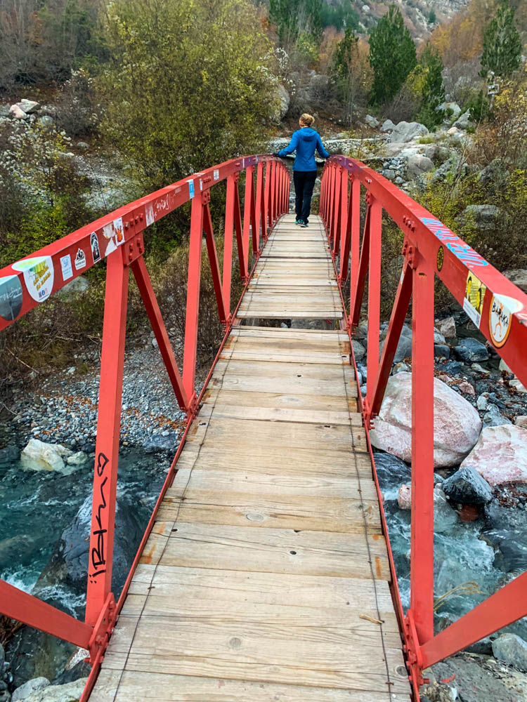 Melanie läuft über eine Brücke, welche über eine Schlucht führt. Die Brücke besteht aus Holzbrettern, wobei einige davon fehlen. Landschaftsaufnahme Albaniens
