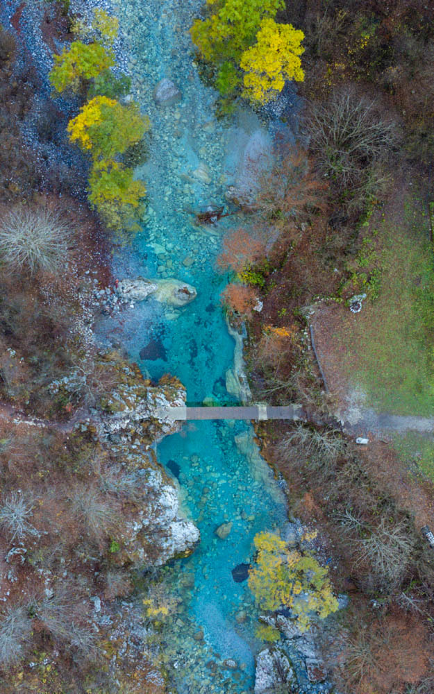 Vogelperspektive von einem Fluss, der umgeben von Bäumen ist. Über den Fluss führt eine Brücke. Nationalpark Theth Albanien