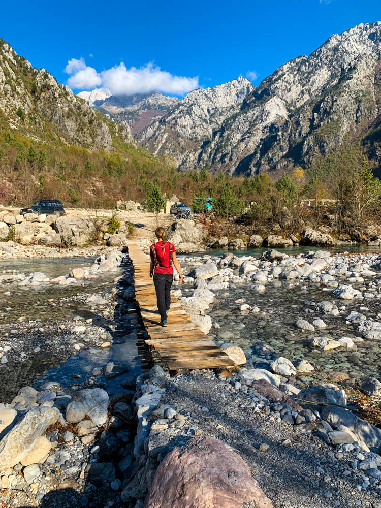 Melanie läuft über eine Holzbrücke, welche über einen Fluss führt. Albanische Gebirgslandschaft bei Theth