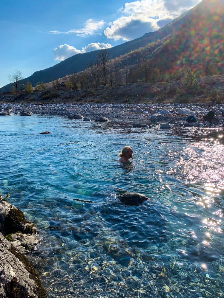 Julian schwimmt in einem eiskalten Fluss im Nationalpark Theth Albanien.Die Sonne schimmert im Wasser.