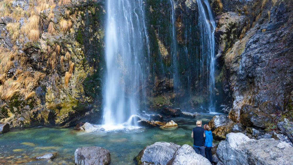 Wasserfall Theth Albanien - Melanie und Julian stehen vor dem Wasserfall und blicken auf ihn. Drohnenaufnahme von vor dem Wasserfall