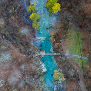 Vogelperspektive von einem Fluss, der umgeben von Bäumen ist. Über den Fluss führt eine Brücke. Nationalpark Theth Albanien