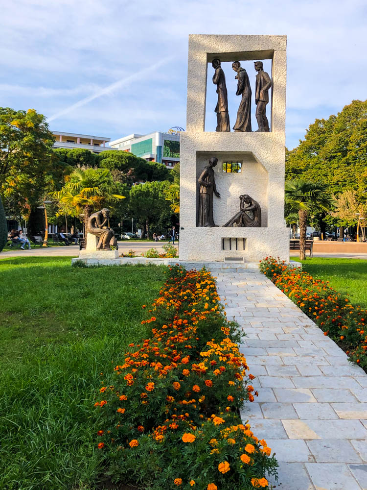 Eine Steinskulptur in Shkodra Albanien steht in einem Park. In der Skulptur sind mehrere Messingfiguren zu sehen