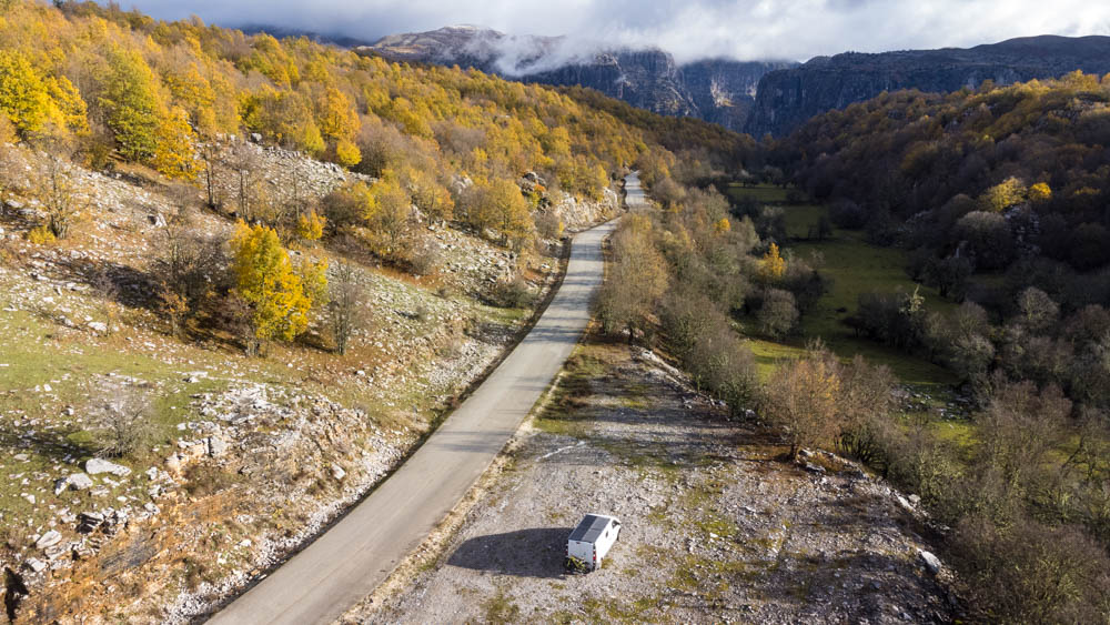 Van Vivaldi steht auf einem Parkplatz neben einer Straße, welche zu einem Aussichtspunkt der Vikos Schlucht führt. Herrlicher Ausblick ins Pindos Gebirge, Bäume gelb verfärbt vom Herbst.