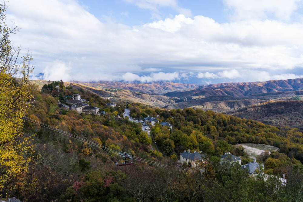 Ein Dorf ist mitten in einem Wald zu sehen. Ansonsten hügelige Landschaft und tolle Herbstfarben im Pindos Gebirge.