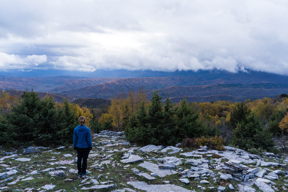 Melanie steht im Stone Forest in Griechenland und blickt in die Ferne ins Pindos Gebirge. Über den Bergen am Horizont hängen ein paar tiefe Wolken.