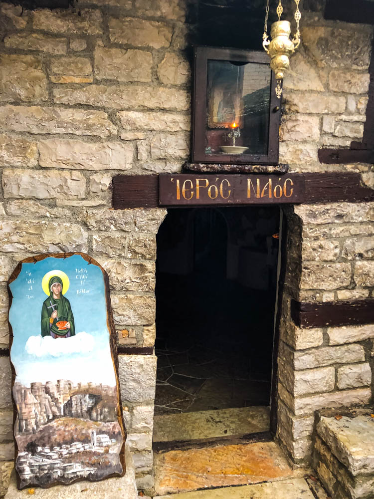 Eingang zu einem Gebäude in einem Kloster in Griechenland. Das Loch in der Wand ist relativ niedrig, sodass sich jeder für den Eintritt bücken muss. Über und neben der Tür sind Gemälde angebracht.