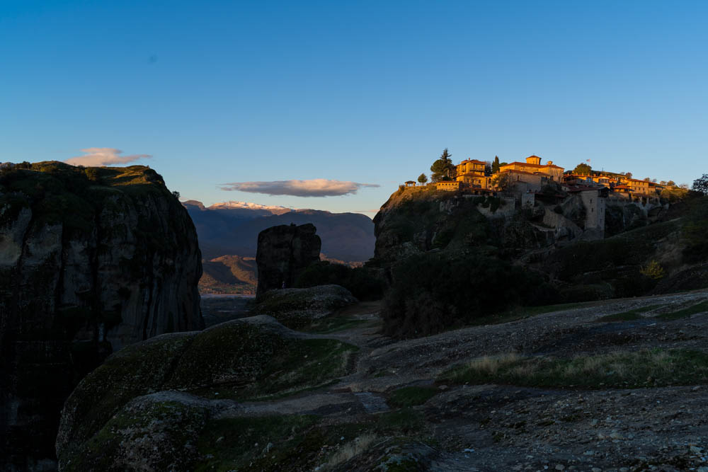 Meteora Kloster in Griechenland bei Sonnenaufgang mit kaum Wolken am Himmel. Das Kloster wird teilweise von der Sonne beschienen.
