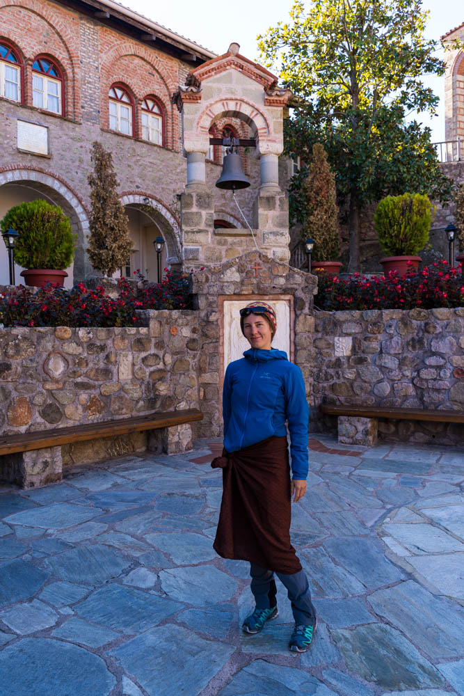 Melanie in einem Meteora Kloster in Griechenland. Sie trägt ein Tuch um ihre Hüften gewickelt, da Hosen bei Frauen nicht so gerne gesehen werden. Innenhof eines Klosters