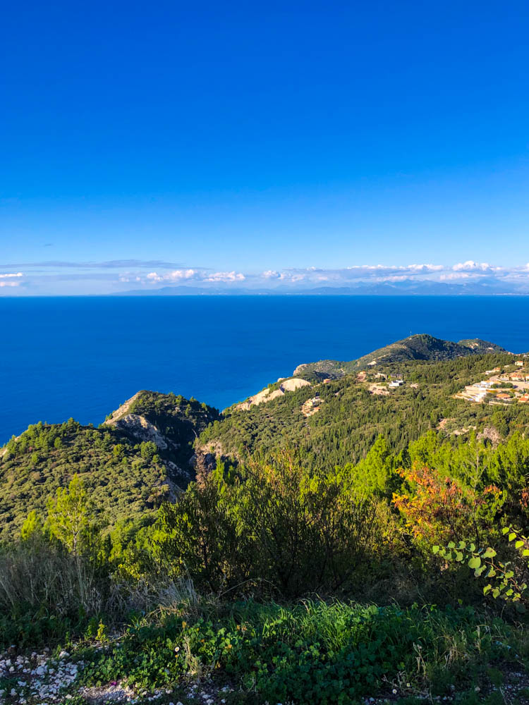 Zur Ruhe kommen auf Lefkada in Griechenland. Saftig grüne Wälder im Gebirge, kräftig blaues Meer dazwischen und auf dem oberen Teil des Bildes den wolkenlosen blauen Himmel.