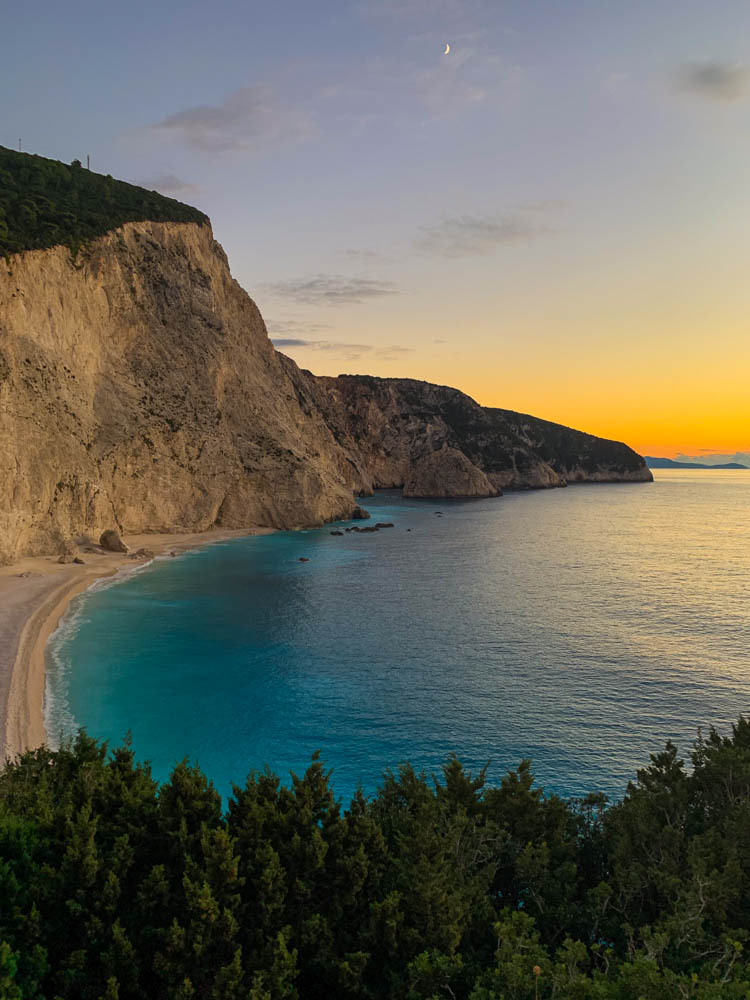 Paradiesische Strandbucht auf Lefkada in Griechenland bei Sonnenuntergang. Der Himmel ist rötlich-orange verfärbt und das Wasser ist türkisfarben. Zur Ruhe kommen im Paradies