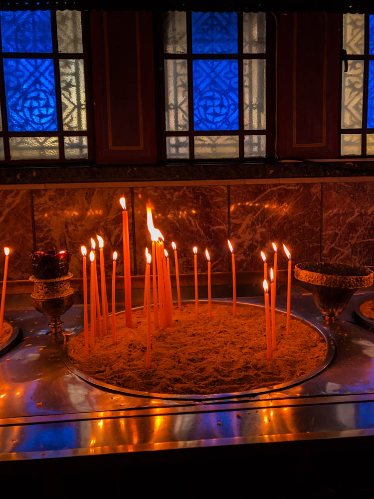 Angezündete Kerzen sowie bunt beleuchtete Glasfenster in der Agios Andreas Kirche in Patras auf der Insel Peloponnes.