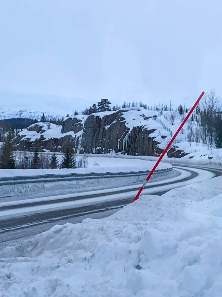 Straßenverhältnisse in Skandinavien im Winter. Im Schnee steckt eine rote Stange, um den Straßenrand zu markieren.