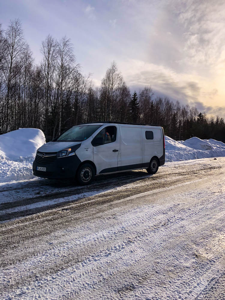 Van Vivaldi steht auf einem Parkplatz im Winter in Skandinavien. Der Himmel ist nur leicht bewölkt und die Sonne kämpft sich durch. Auf der Straße ist Schnee und Eis zu erkennen.