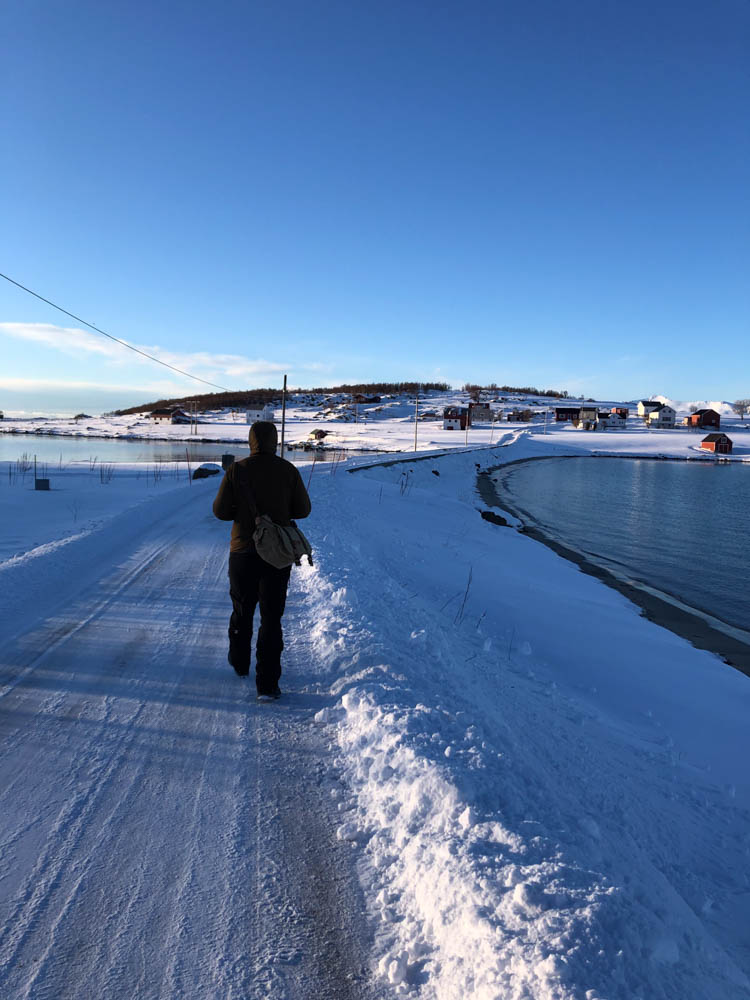 Julian läuft auf einer vereisten Straße in Skandinavien im Winter. Straßenverhältnisse aus checken. Der Himmel ist kräftig blau.