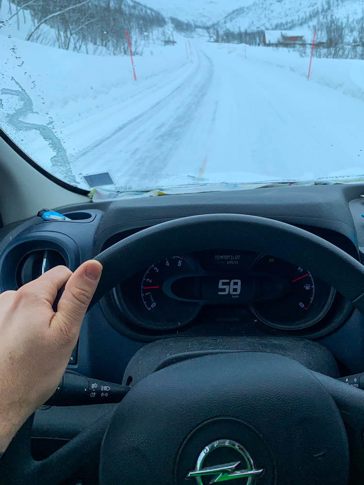Straßenverhältnisse in Skandinavien im Winter. Aufnahme im Fahrzeugcockpit auf Lenkrad bzw. Geschwindigkeitsanzeige sowie vereiste Straße. Es ist gerade am schneien