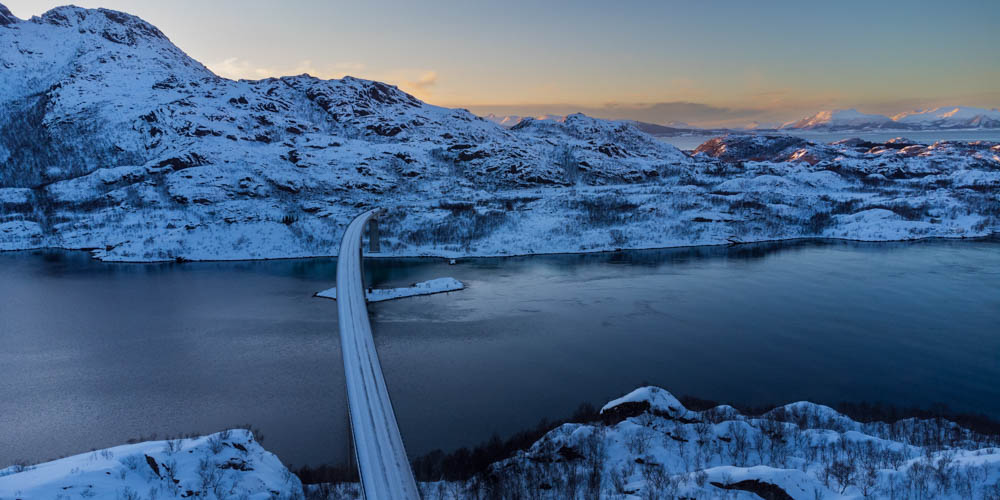 Winterlandschaft in Skandinavien. Eine vereiste Brücke führt über einen Fjord. Sonnenuntergang im Winter.