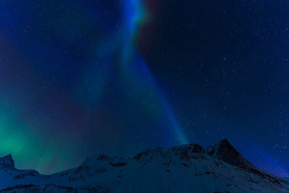Nordlichter auf Senja (Norwegen) fotografiert. Es tanzen blaue sowie grüne Lichter am Himmel, welcher voller Sterne ist. Blick auf verschneite Berge - Skandinavien im Winter.