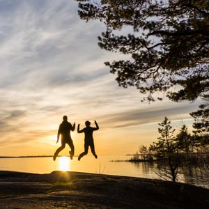 Melanie und Julian springen gleichzeitig in die Luft. Hinter ihnen geht die Sonne unter und leuchtet die beiden an. Naturreservat in Schweden - sehenswerte Reiseziele