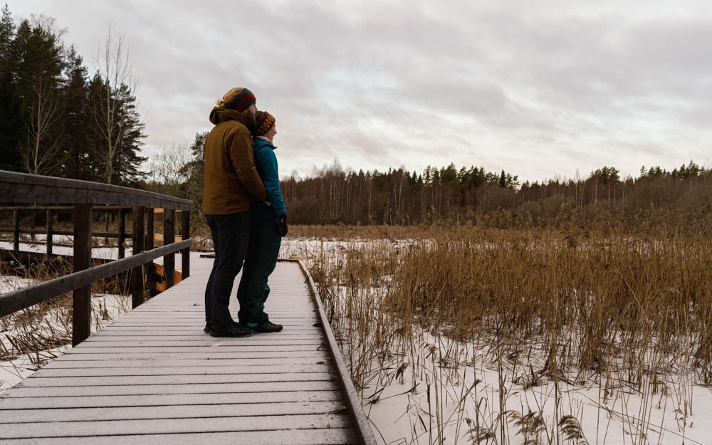 Sehenswerte Reiseziele - Färnebofjärdens Nationalpark in Schweden. Melanie und Julian blicken auf die tolle Landschaft im Park und stehen dabei auf einem verschneiten Steg.