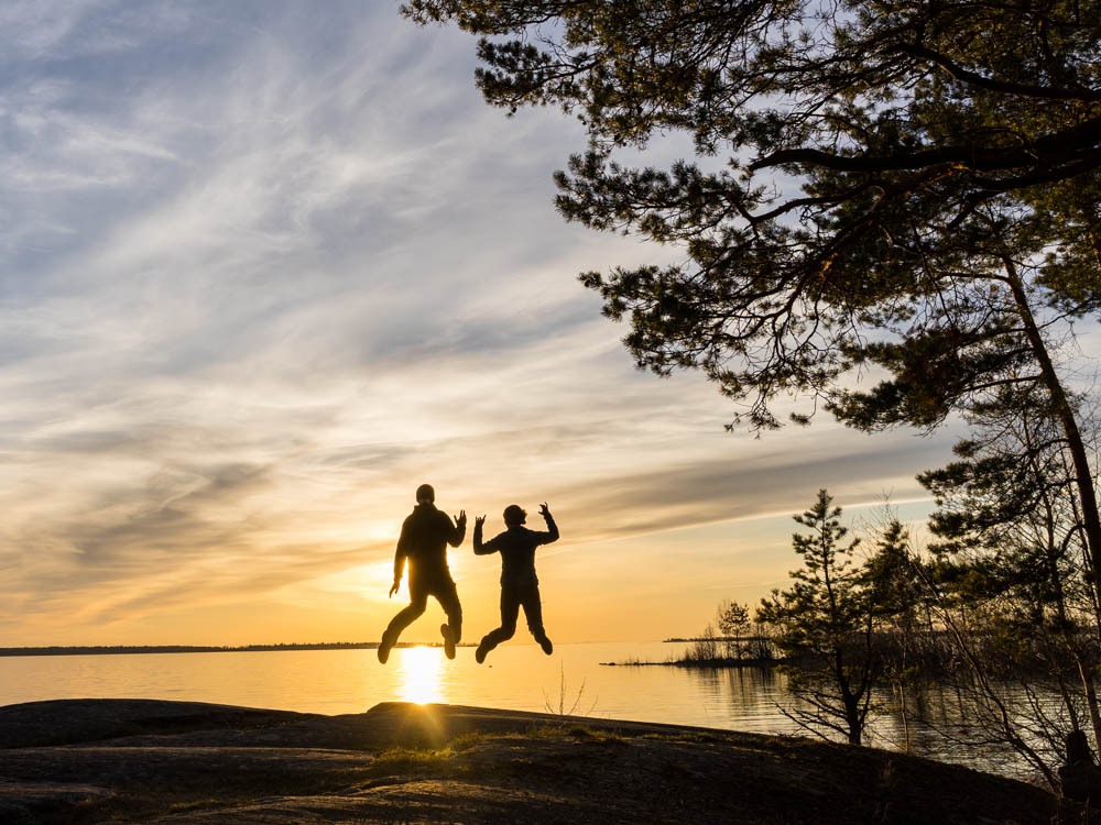 Melanie und Julian springen gleichzeitig in die Luft. Hinter ihnen geht die Sonne unter und leuchtet die beiden an. Naturreservat in Schweden - sehenswerte Reiseziele