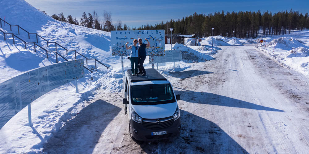 Sehenswerte Reiseziele in Schweden: Der Polarkreis! Melanie und Julian stehen auf der Dachterrasse ihres Vans und ihre Drohne macht hiervon ein Aufnahme.