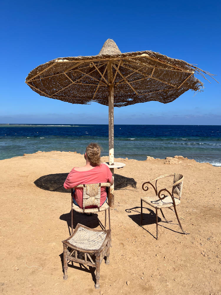 Julian sitzt am Strand in Ägypten und blickt auf das Meer. Der Himmel ist kräftig blau.