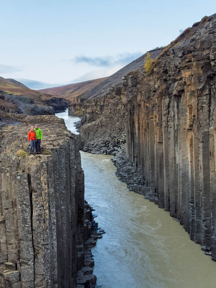 Stuðlagil Canyon mit Basaltsäulen in Island im Herbst. Melanie und Julian stehen auf den Säulen, unter ihnen verläuft ein Fluss.