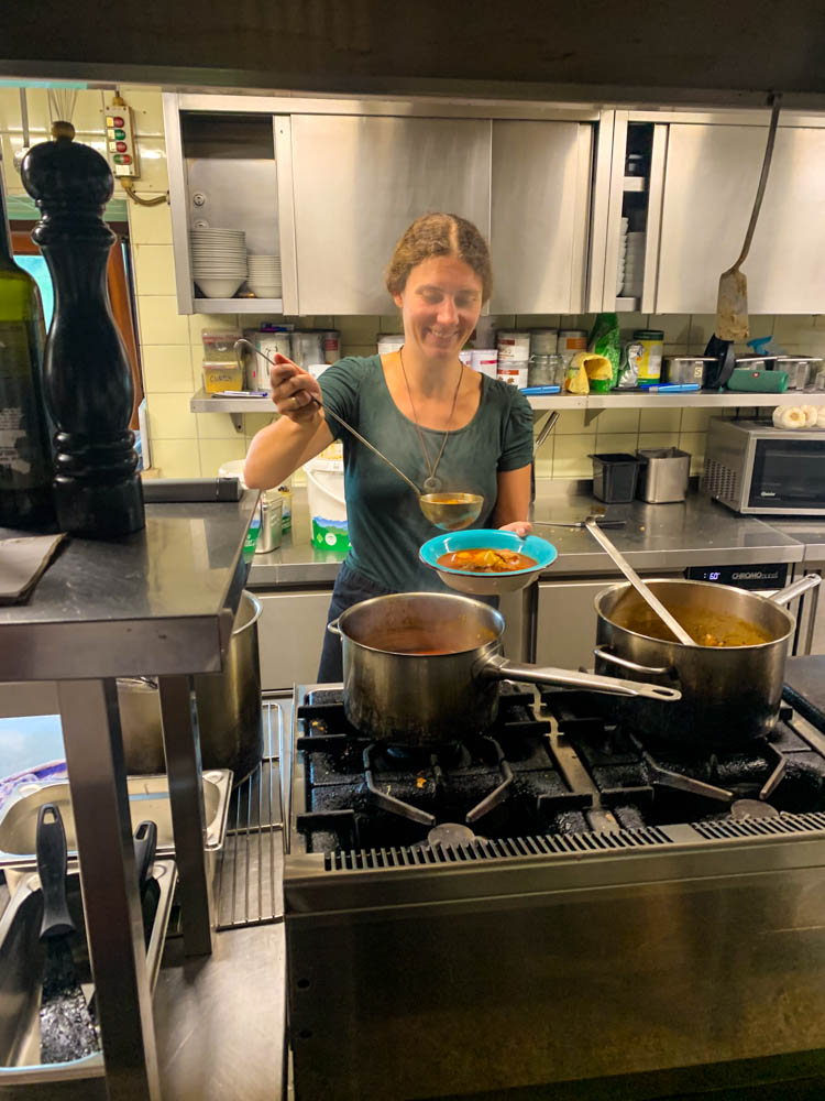 Melanie schöpft eine Suppe auf Priener Hütte aus und hat offensichtlich Spaß bei der Arbeit. Saisonarbeit auf Alpenvereinshütte. 5 Jahre Entscheidung zur Weltreise