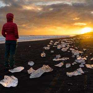 Melanie steht am Diamond Beach in Island im Herbst und beobachtet den Sonnenuntergang. Es liegen kleinere Eisbrocken am Strand, welche von der untergehenden Sonne angestrahlt werden. 5 Jahre Entscheidung zur Weltreise