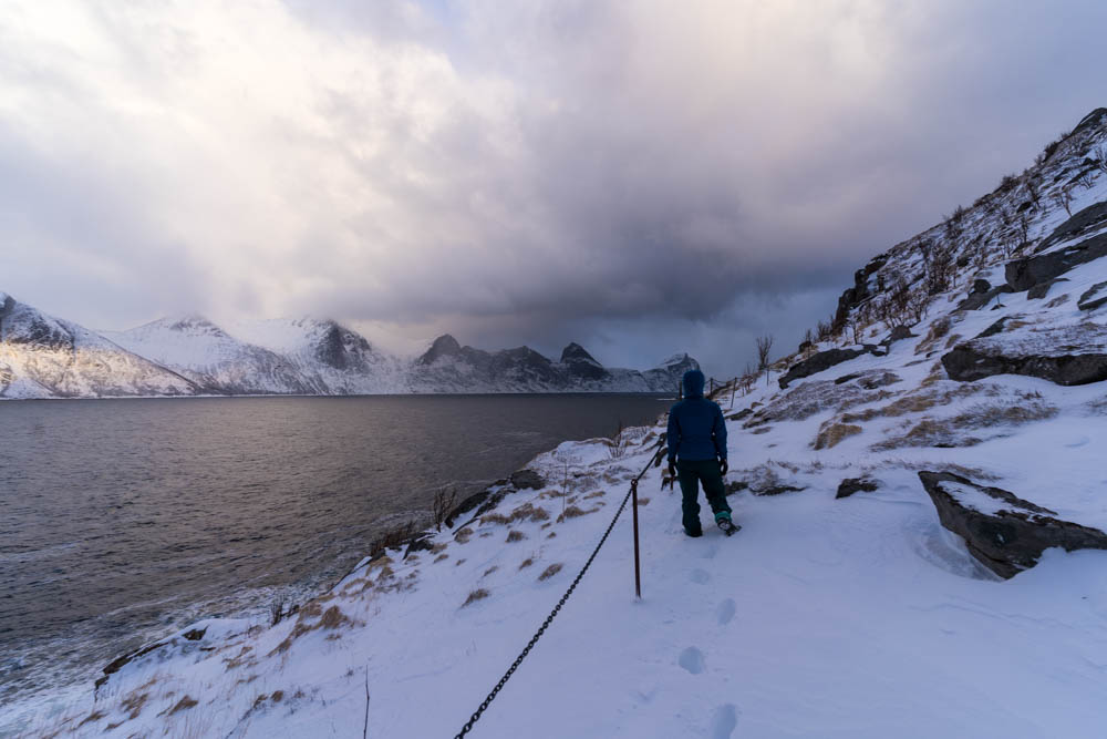 Melanie bei Schneewanderung an Küste auf Insel Senja in Norwegen. Blick in einen Fjord und auf die Berge.