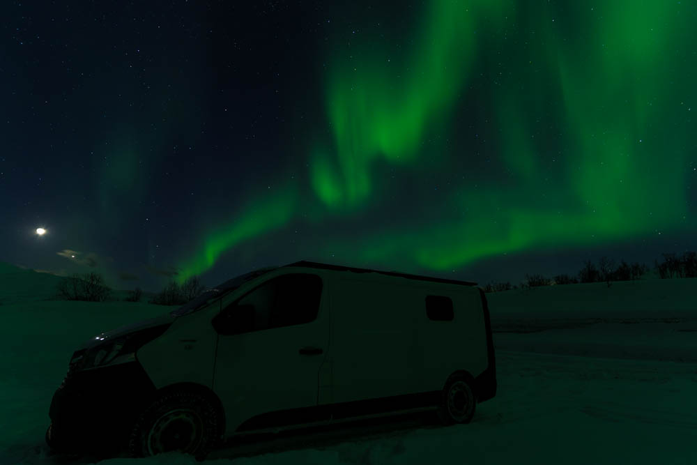 Grüne, tanzende Aurora Borealis über Schneelandschaft und Van Vivaldi. Nordlichter und Tourengehen in Norwegen auf Senja