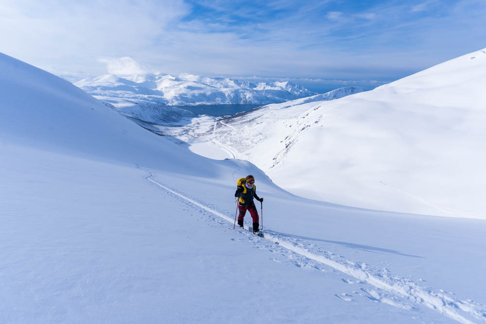 Melanie im Aufstieg beim Tourengehen. Blick auf Schneelandschaft in den Bergen und Fjord. Senja, Norwegen