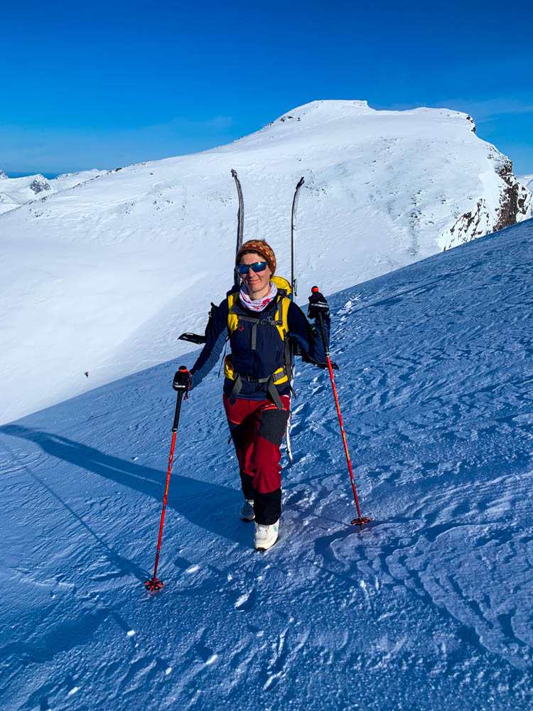 Melanie bei Aufstieg bei Skitour. Ihre Splitboards hängen rechts und links am Rucksack, da der Weg zu vereist war. Tourengehen auf Senja bei kräftig blauem Himmel