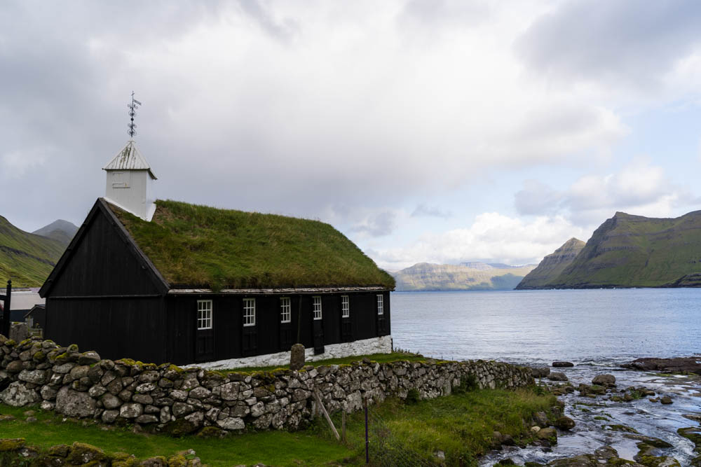 Kirche mit Grasdach am Meer gelegen. Wunderschöne Hügellandschaft der Küste entlang zu sehen. Mit dem Camper auf die Färöer Inseln