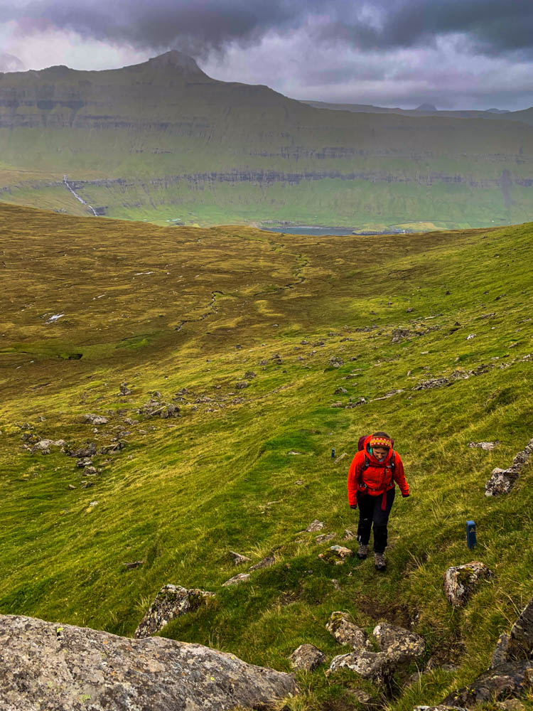 Wanderung von Hellurnar nach Fuglafjørður. Melanie auf kaum sichtbaren Wegen durch Graslandschaft bei regnerischen Bedingungen. Mit dem Camper auf die Färöer Inseln und die Inseln zu Fuß erkunden