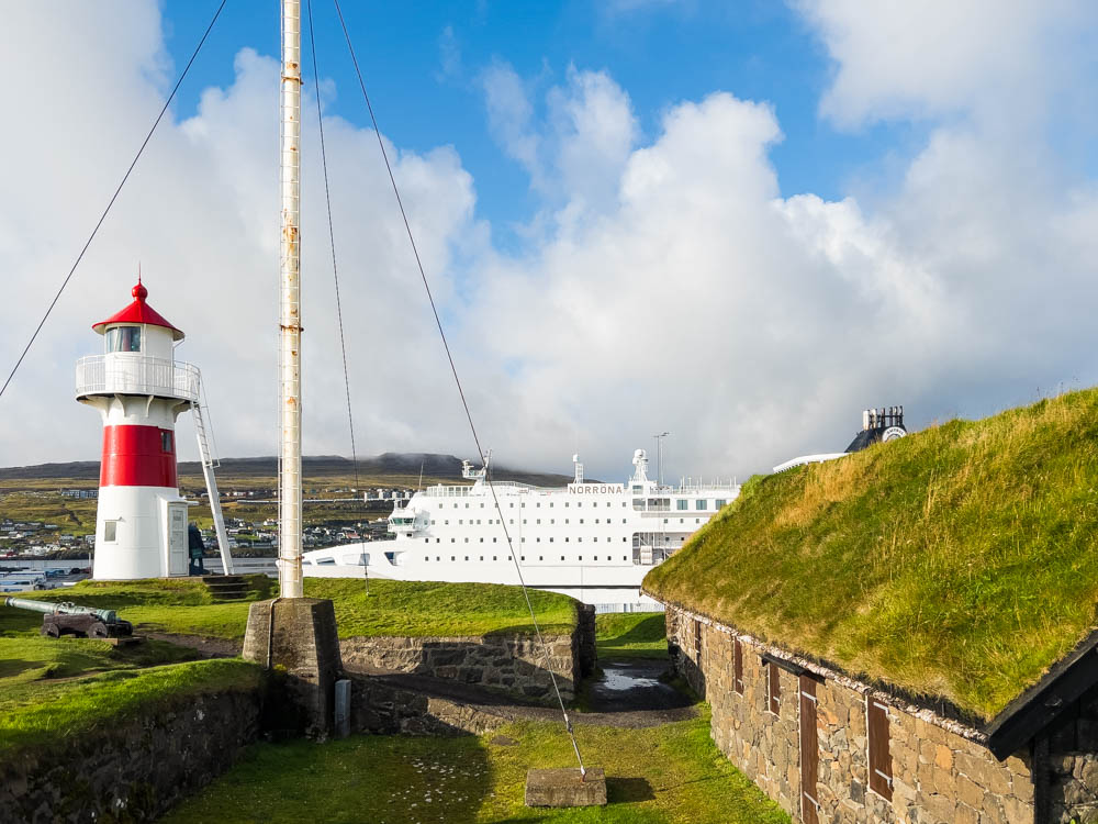 Alte Hafenfestung Skansin mit Leuchtturm und Steinhaus mit Grasdach bei Hauptstadt Tórshavn. Mit dem Camper auf die Färöer Inseln - Anreise mit Fähre, welche auf dem Bild ebenfalls zu sehen ist.