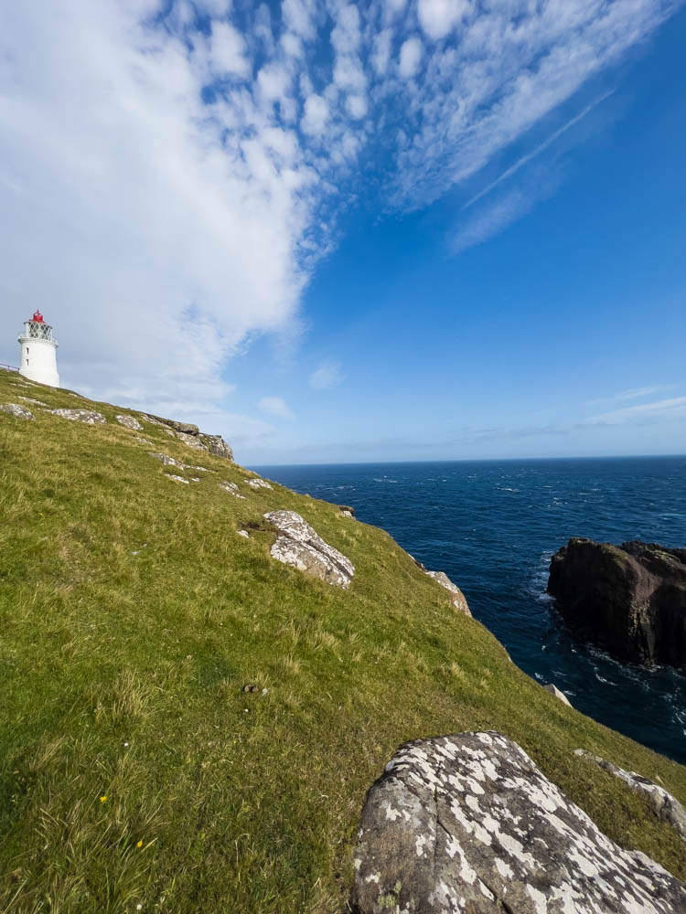 Leuchtturm auf Insel Nólsoy, eine der Färöer Inseln. Klippe und Meer bei teilweise blauem Himmel