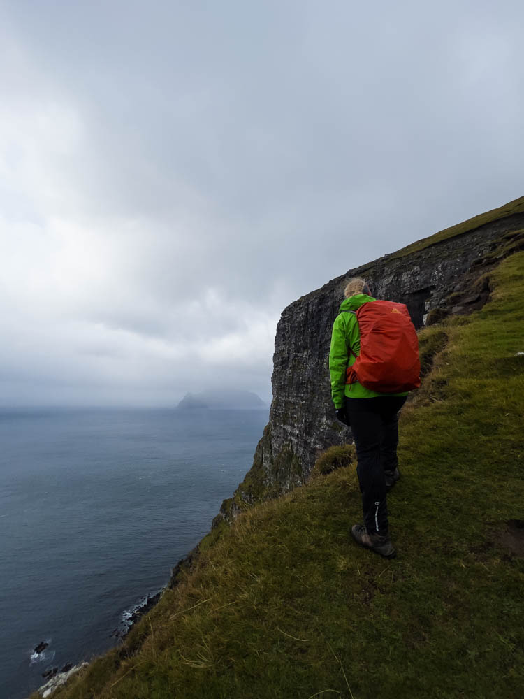 Wanderung auf alter Postroute von Bøur nach Gásadalur auf Insel Vágar der Färöer Inseln. Julian bei Steilküste. Der Nebel hängt über dem Meer und man erkennt schwach eine Insel im Atlantik. Inselerkundung mit dem Camper und zu Fuß