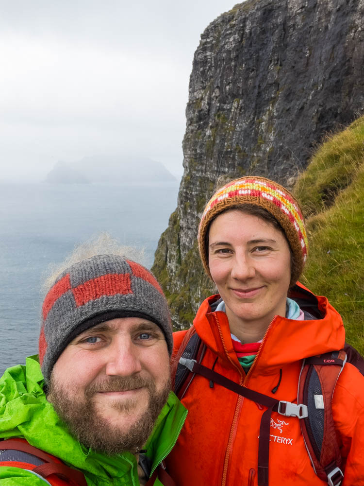 Wanderung auf alter Postroute von Bøur nach Gásadalur auf Insel Vágar der Färöer Inseln. Selfie von Melanie und Julian bei Steilküste. Der Nebel hängt über dem Meer und man erkennt schwach eine Insel im Atlantik. Inselerkundung mit dem Camper und zu Fuß