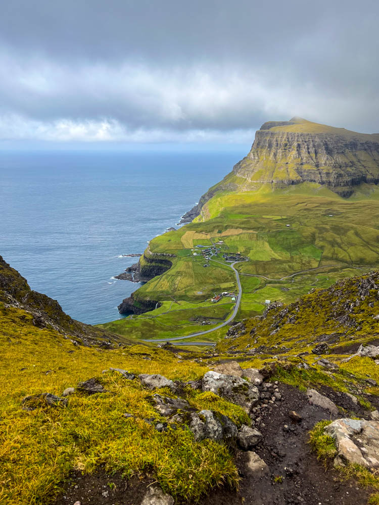 Wanderung auf alter Postroute von Bøur nach Gásadalur auf Insel Vágar der Färöer Inseln. Blick von Anhöhe bei Abstieg nach Gásadalur und auf das Meer. Mit dem Camper auf die Färöer Inseln