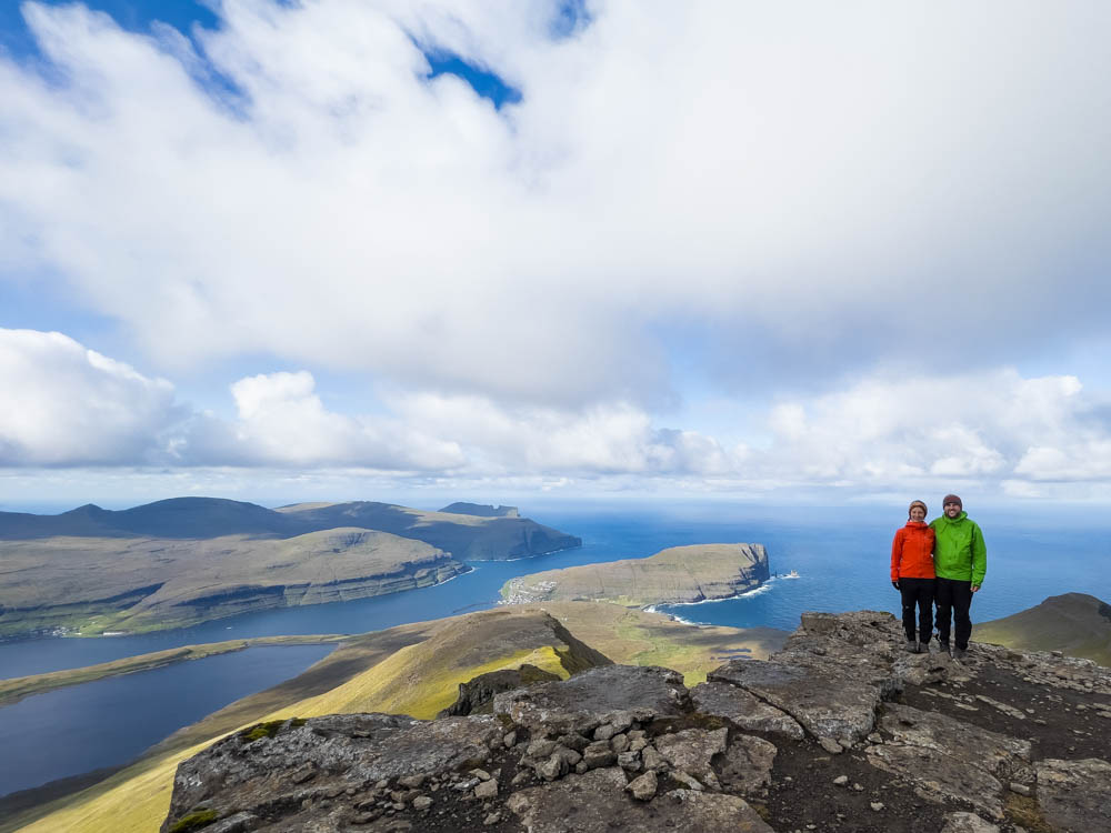 Melanie und Julian auf dem höchsten Berg der Färöer Slættaratindur. Hinter ihnen sind das Meer und einige Fjorde zu sehen. Mit dem Camper auf die Färöer Inseln für Naturliebhaber ein Traum