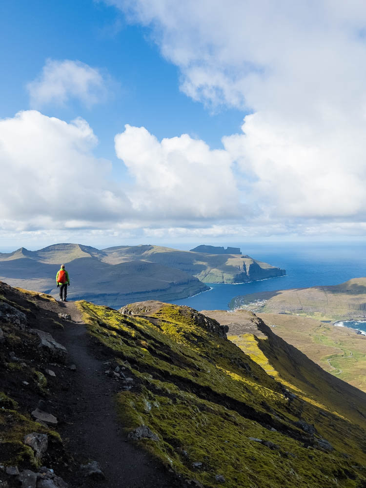 Julian bei einer Wanderung auf den Färöer Inseln mit Blick auf das Meer und viele grüne Hügel.