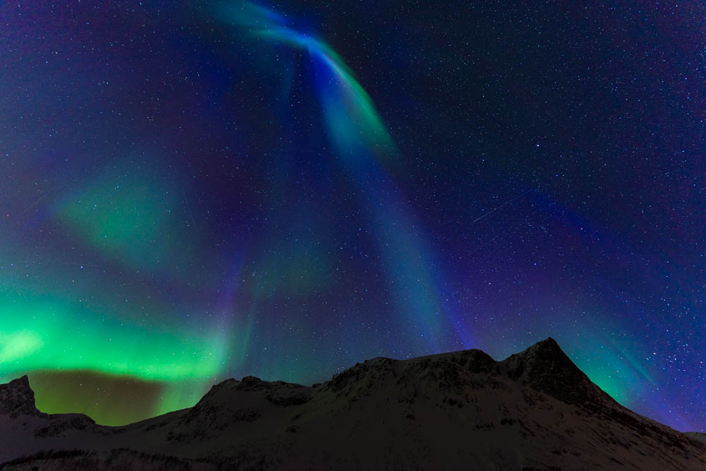 Blaue, violette und grüne Polarlichter über einer Bergkette in Senja, Norwegen. Sternenhimmel und Faszination Nordlichter
