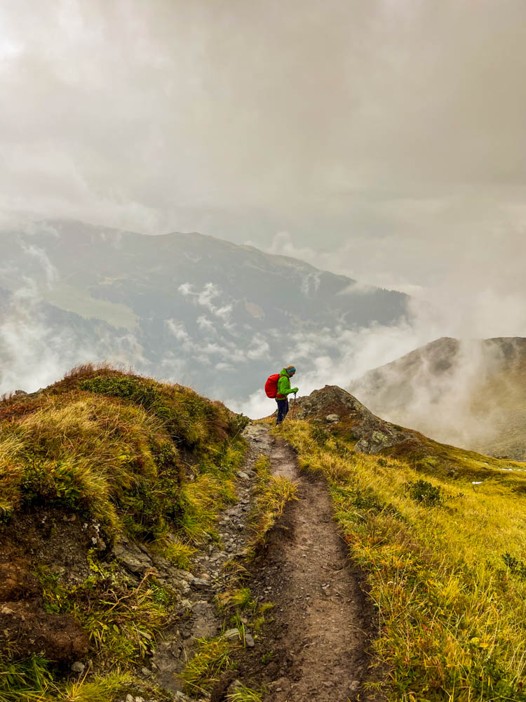 Julian bei einer Tageswanderung in den Alpen. Wolken ziehen aus dem Tal nach oben. Packliste für eine Wanderung
