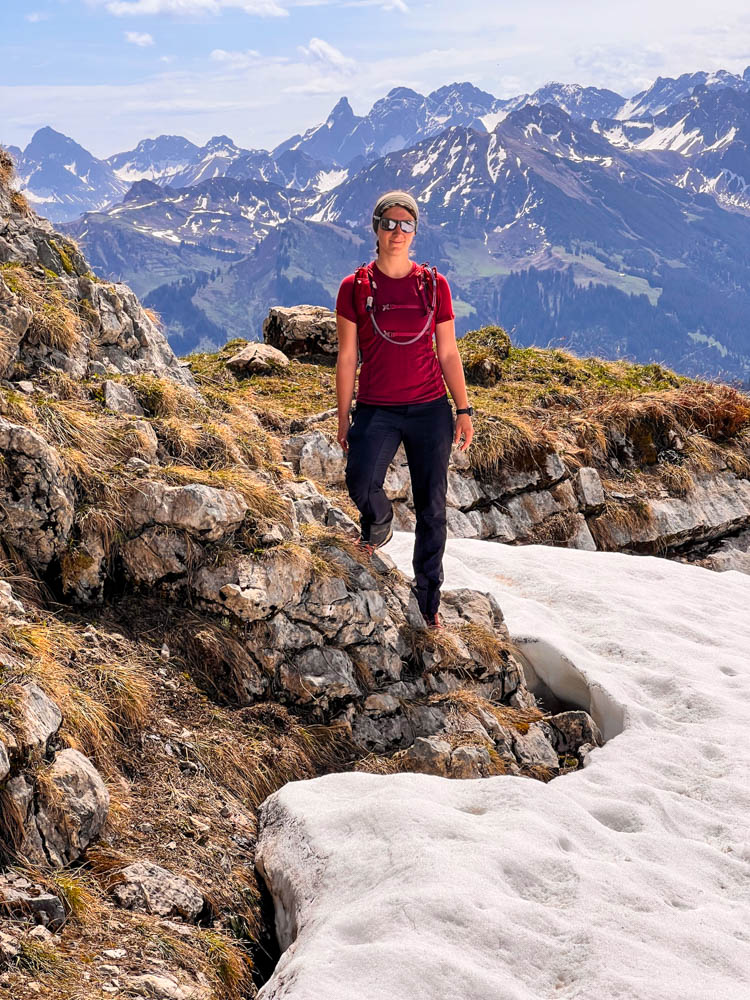 Melanie bei einer Wanderung in den Alpen. Sie trägt eine Trailrunning-Weste und grinst in die Kamera. Packliste für eine Tageswanderung