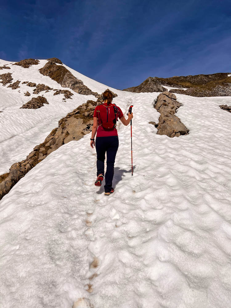 Melanie wandert durch ein Altschneefeld und trägt eine Trailrunning-Weste. Der Himmel ist blau. Packliste für eine Tageswanderung